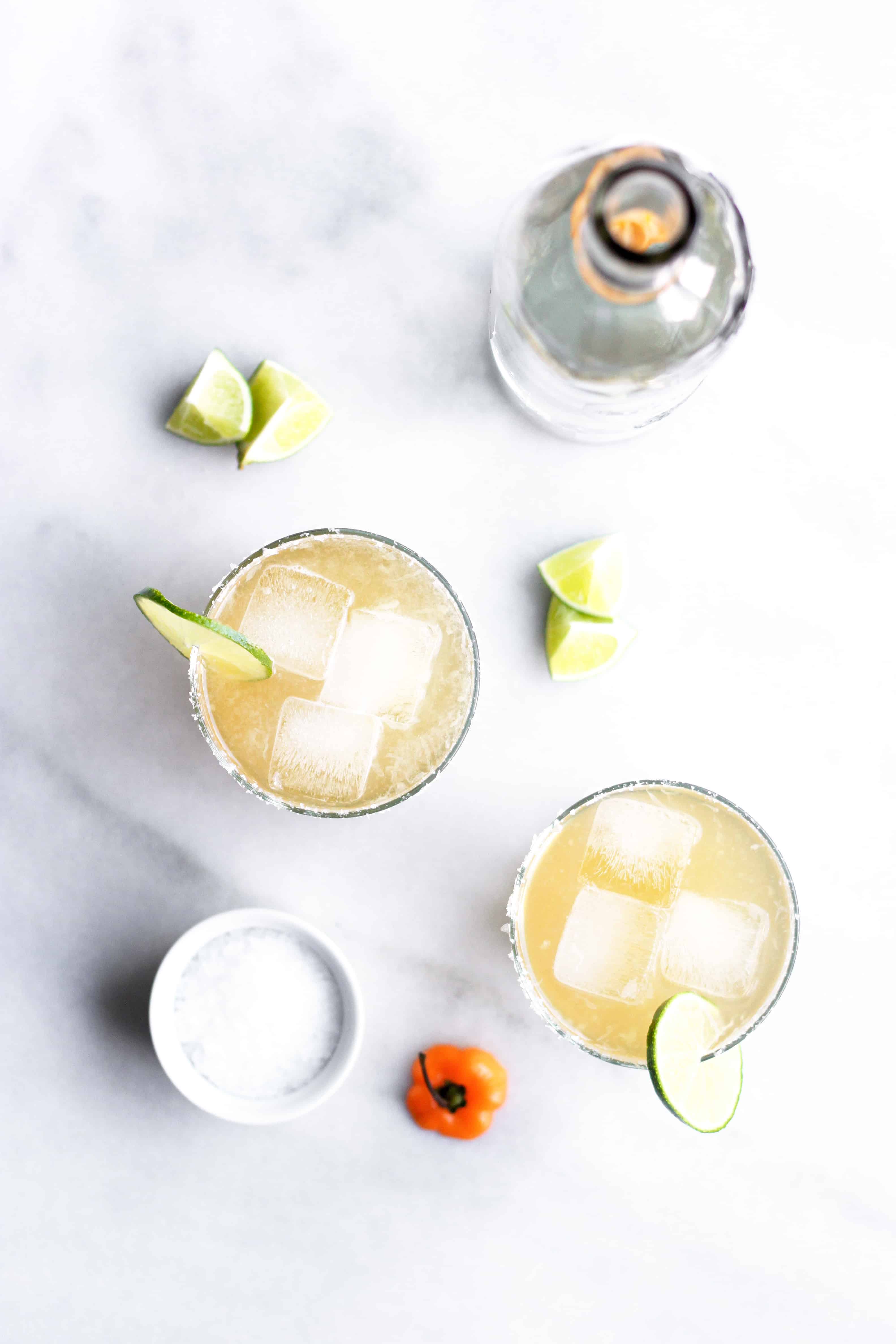 Spicy habanero ginger beer margarita in glass with ice, lime, salted rim and bottle of tequila