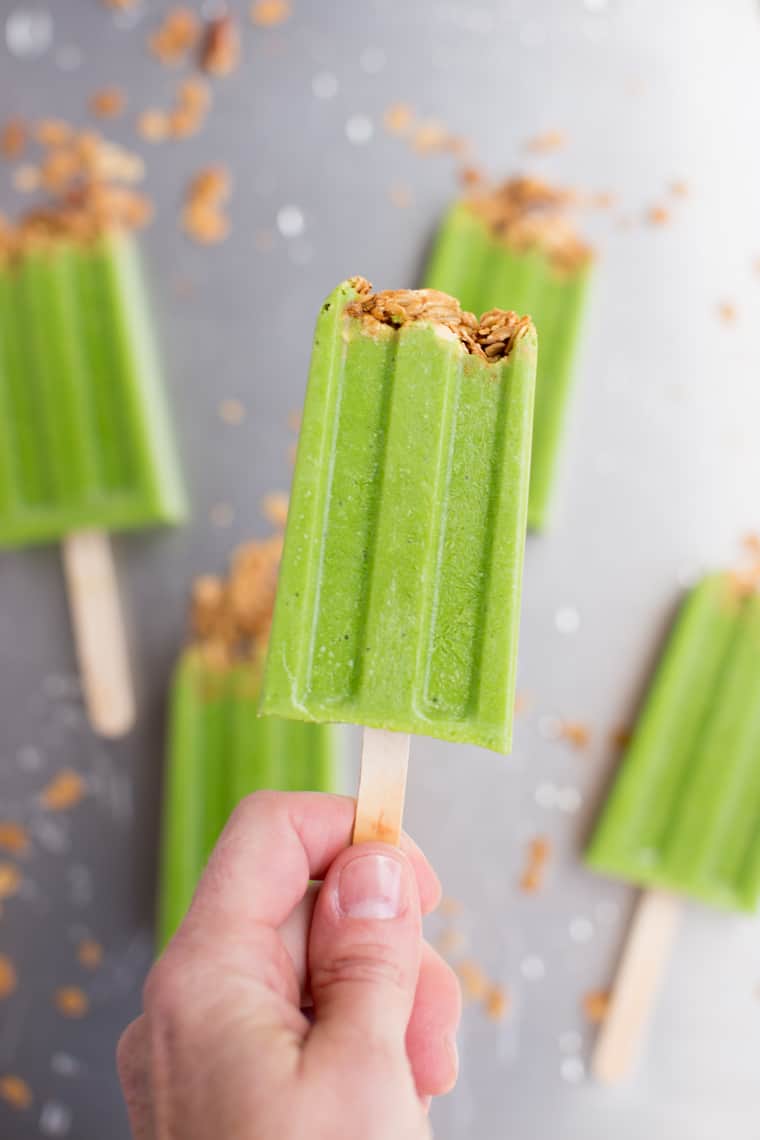 hand holding healthy green smoothie popsicle with crunchy granola topping
