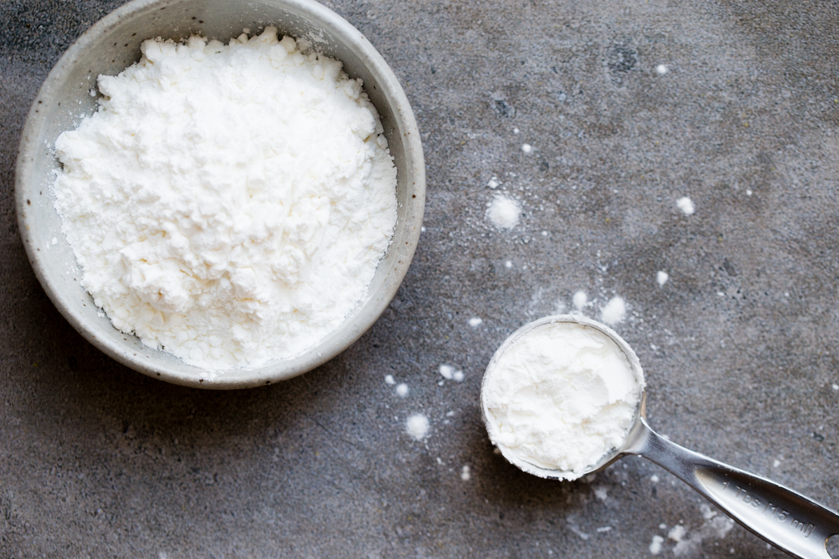 overhead photo of cornstarch in a measuring spoon beside a small bowl of cornstarch 